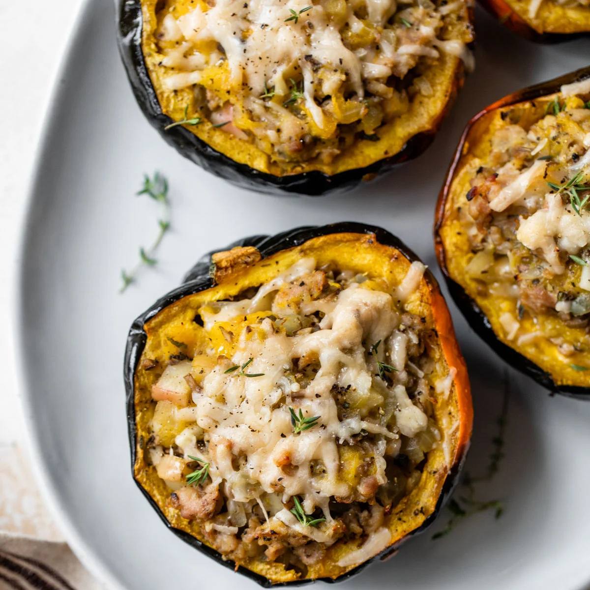 A plate of three stuffed acorn squash halves with a savory filling topped with melted cheese.