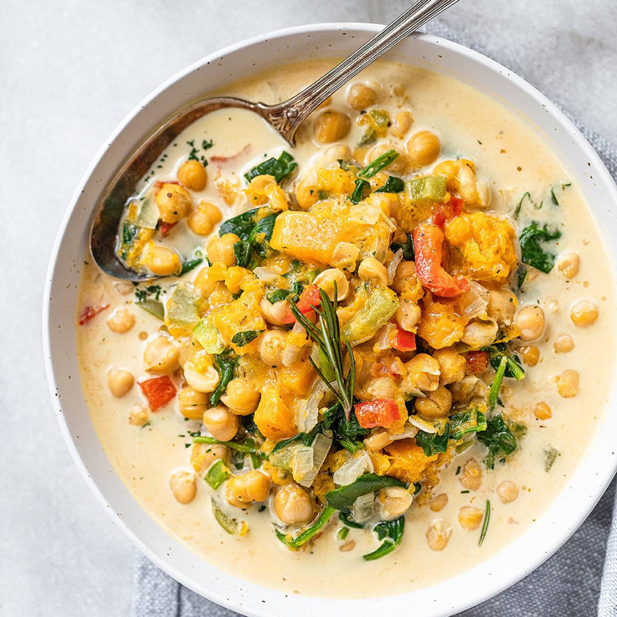 A bowl of creamy chickpea and butternut squash soup with spinach and vegetables.