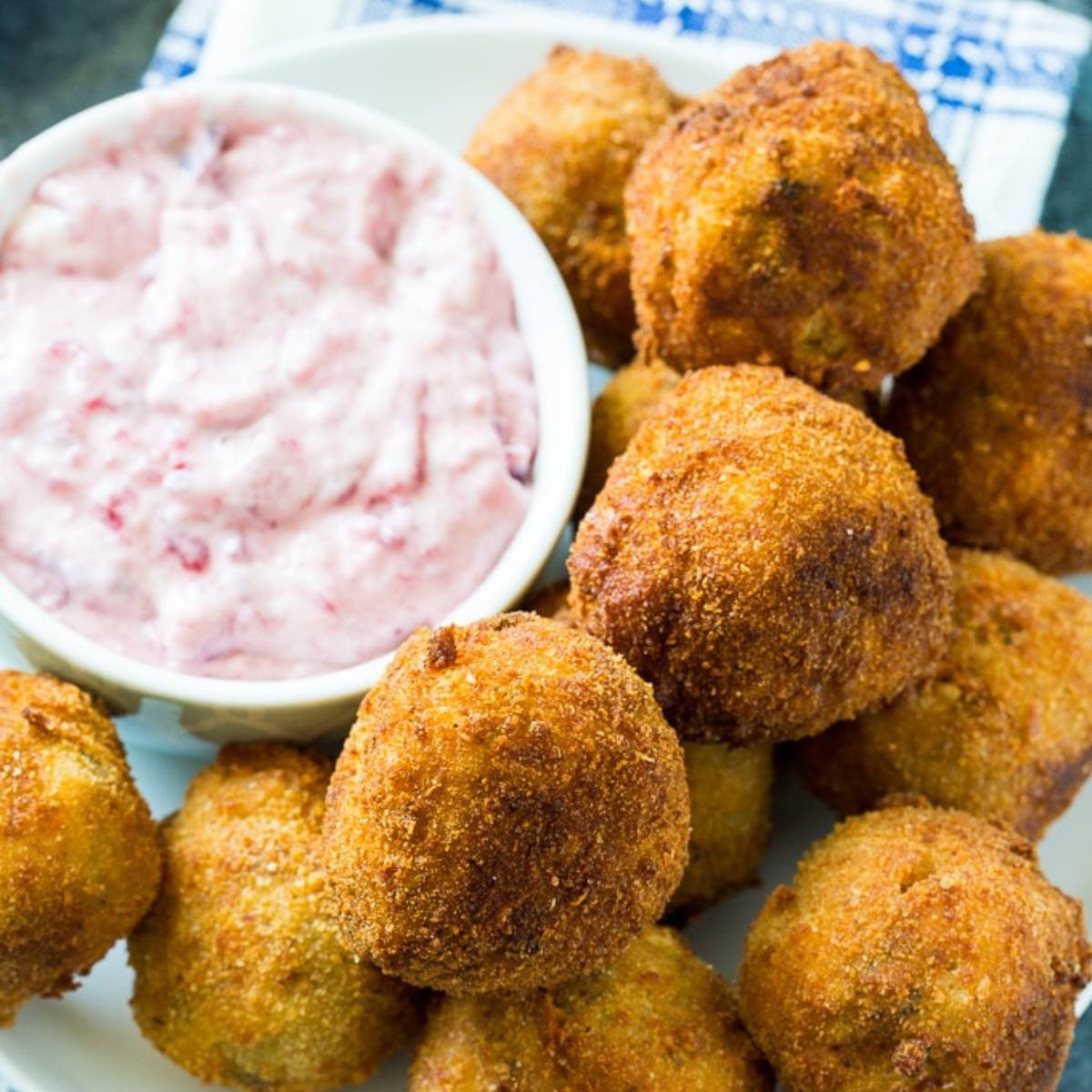 A plate of crispy fried balls with a side of pink dipping sauce.