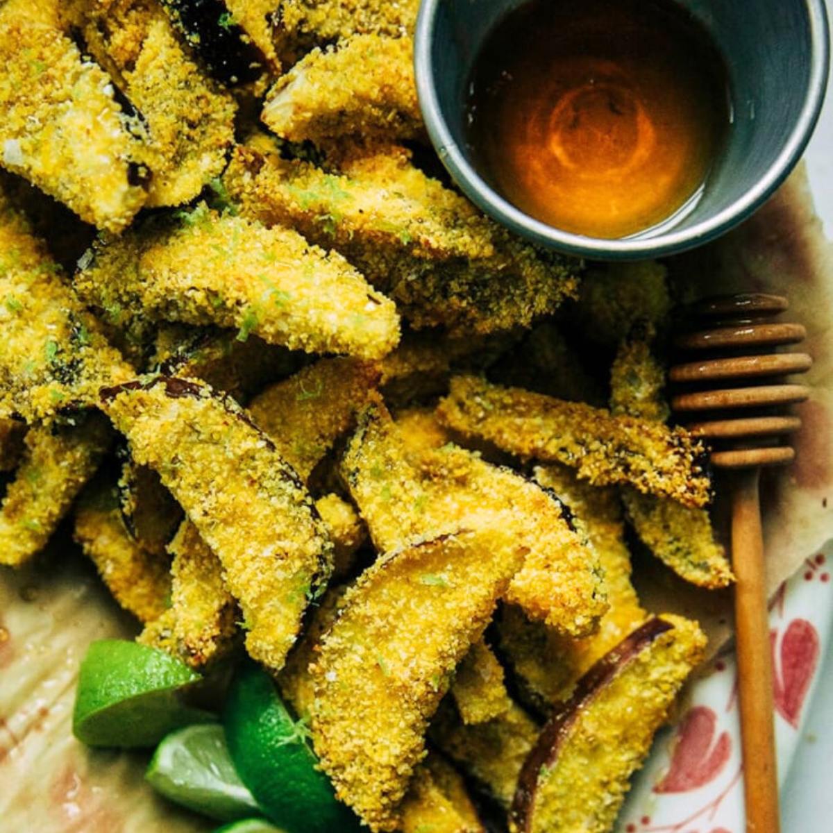 A plate of crispy, golden-brown fried avocado wedges with a side of honey for dipping.