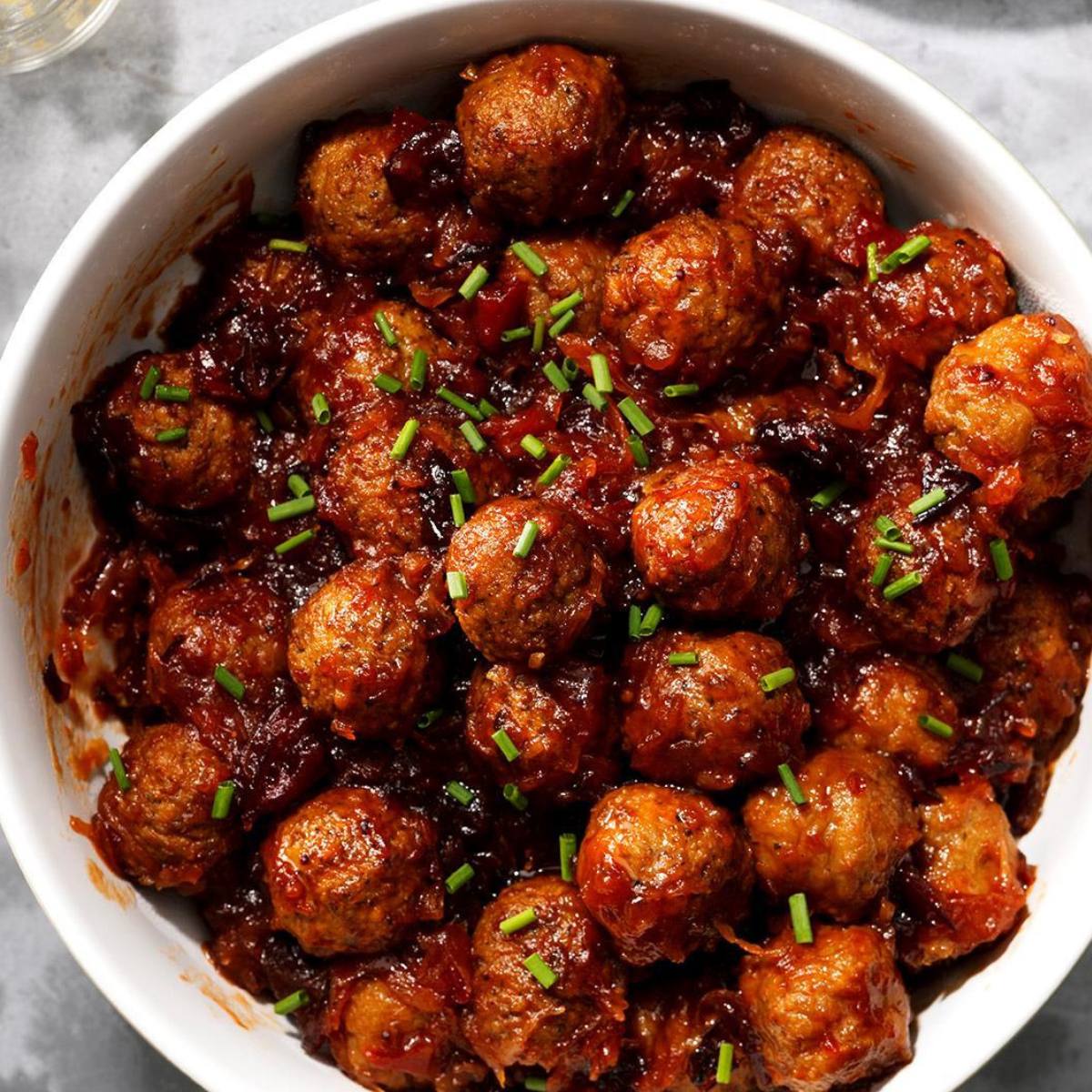 A bowl of meatballs covered in a sweet and tangy sauce, garnished with fresh chives.