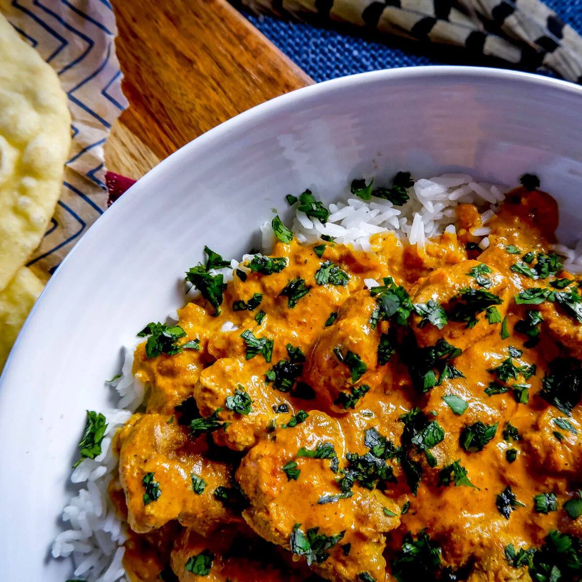 A bowl of delicious-looking butter pheasant. The pheasant is tender and covered in a rich, creamy sauce. The dish is served with a side of fluffy white rice and a piece of naan bread.