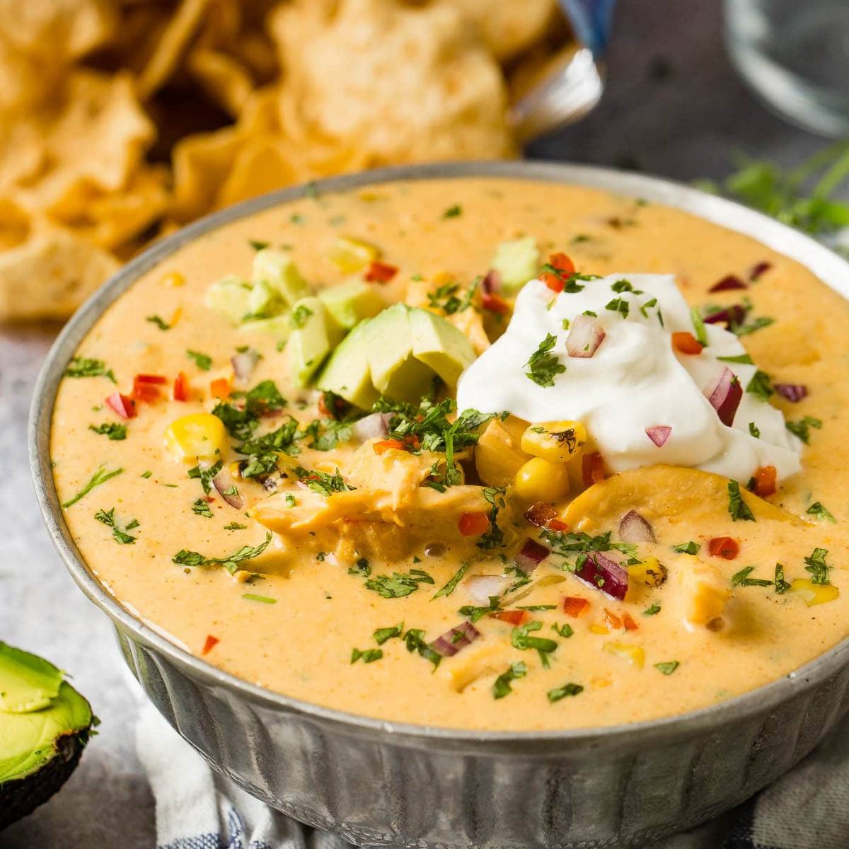 A bowl of creamy, cheesy chicken dip with avocado, sour cream, cilantro, and red pepper flakes. 