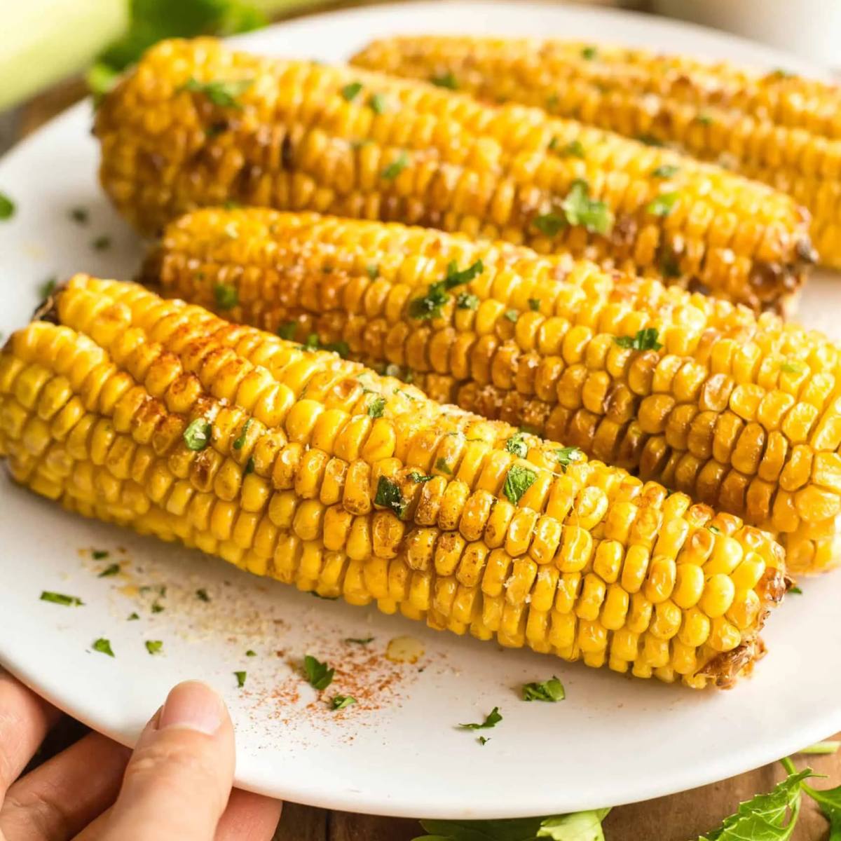 A plate of golden-brown roasted corn on the cob, garnished with fresh parsley.