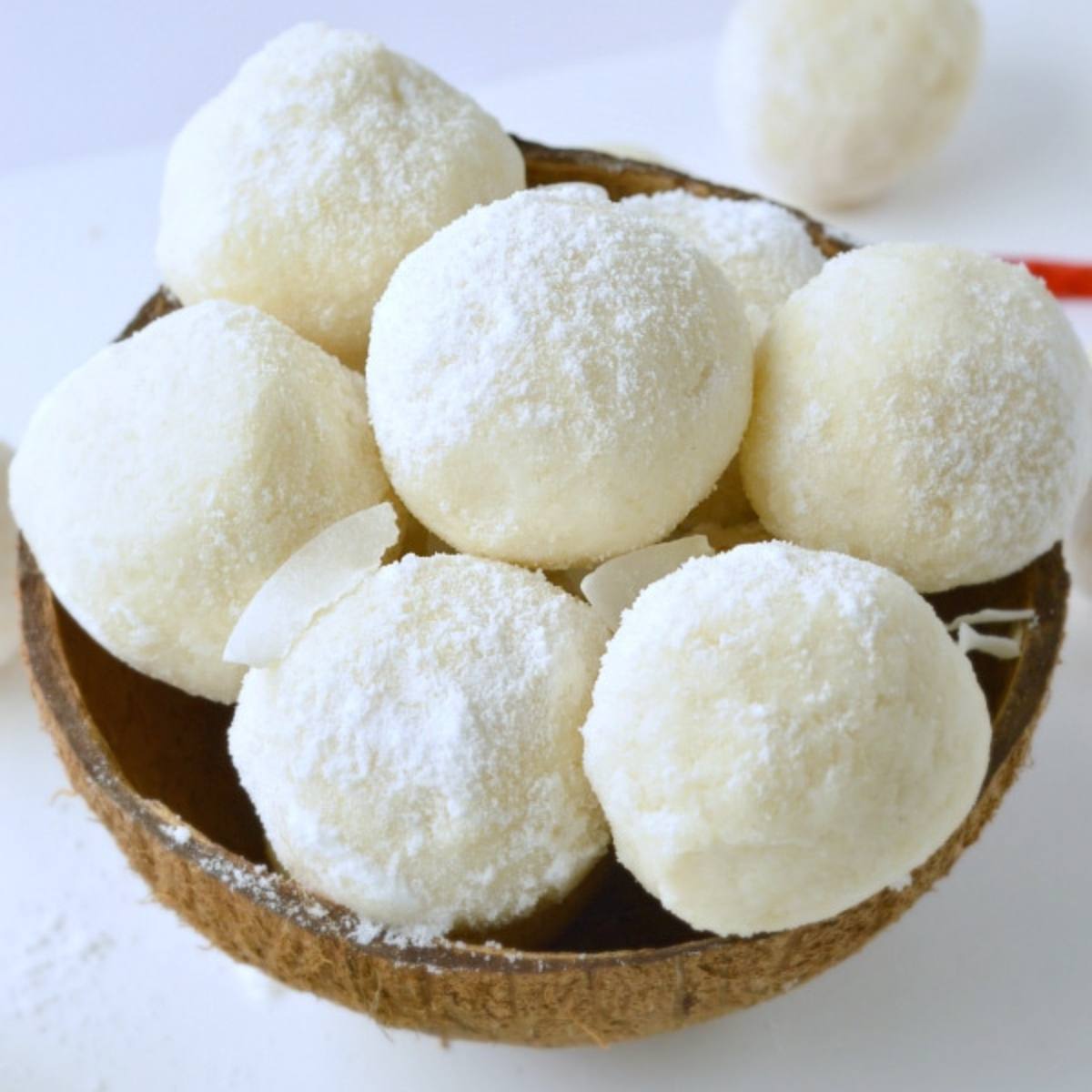 A bowl of coconut snowballs. The snowballs are round and coated in powdered sugar.