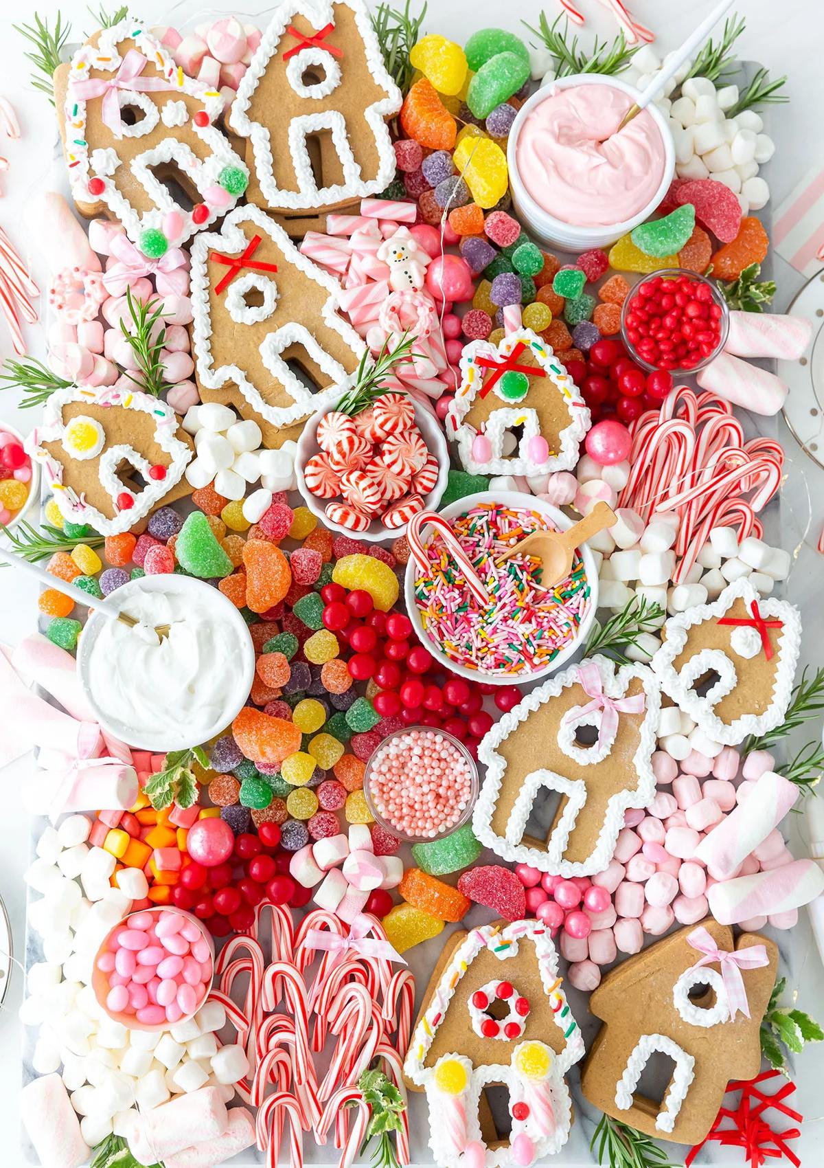 A festive gingerbread house decorating board filled with an assortment of candies, frosting, and gingerbread house cutouts. The board includes various types of candies, such as gumdrops, sprinkles, and candy canes, as well as bowls of frosting for decorating.