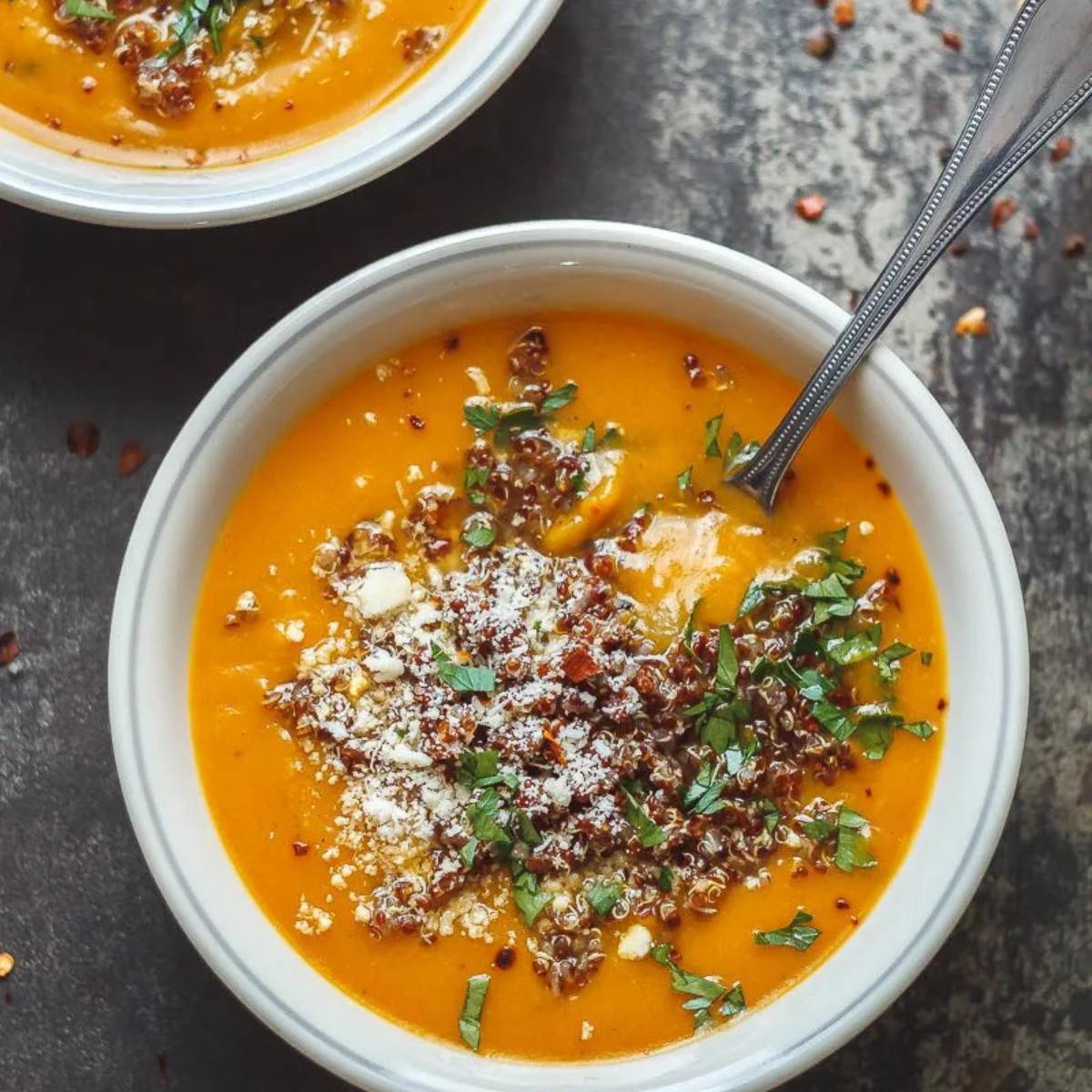 A bowl of creamy butternut squash soup topped with crunchy quinoa and herbs.