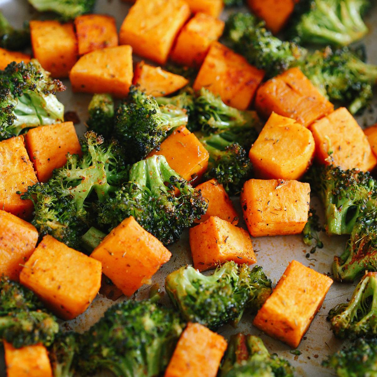 A close-up of roasted sweet potato cubes and broccoli florets, seasoned with herbs and spices.