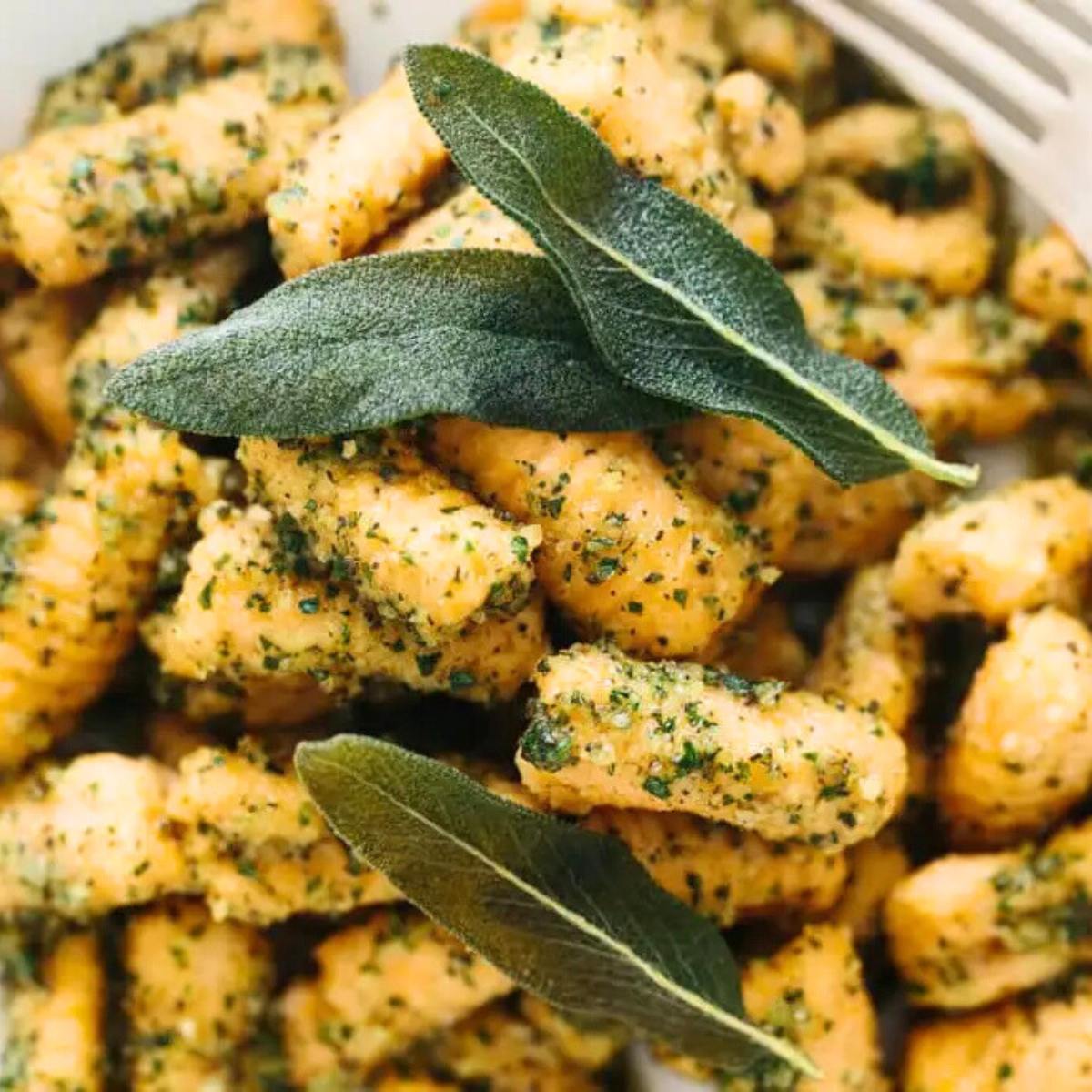 A plate of golden-brown gnocchi topped with a sage pesto and fresh sage leaves.