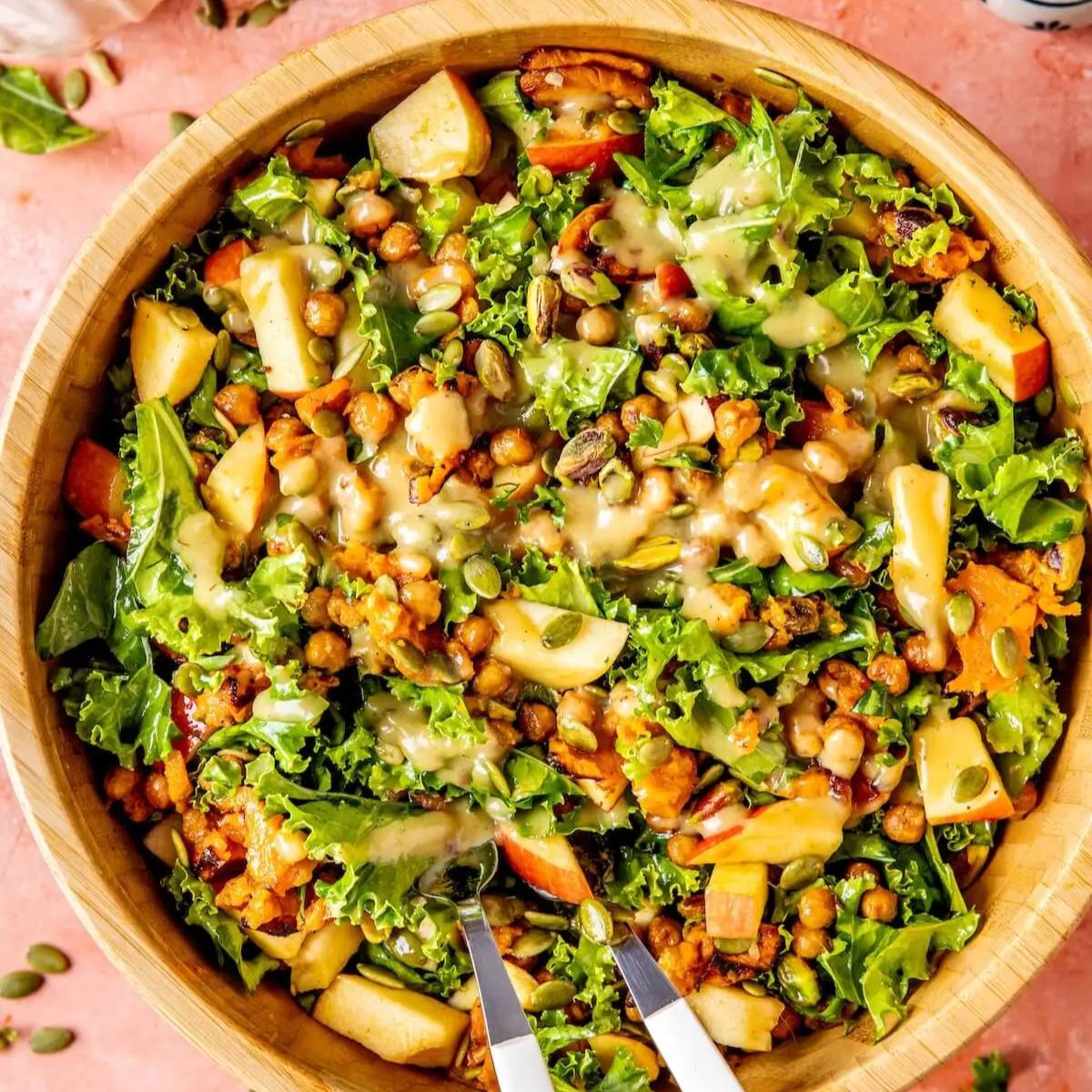 A colorful salad with kale, roasted sweet potatoes, apples, chickpeas, pistachios, and a creamy dressing.