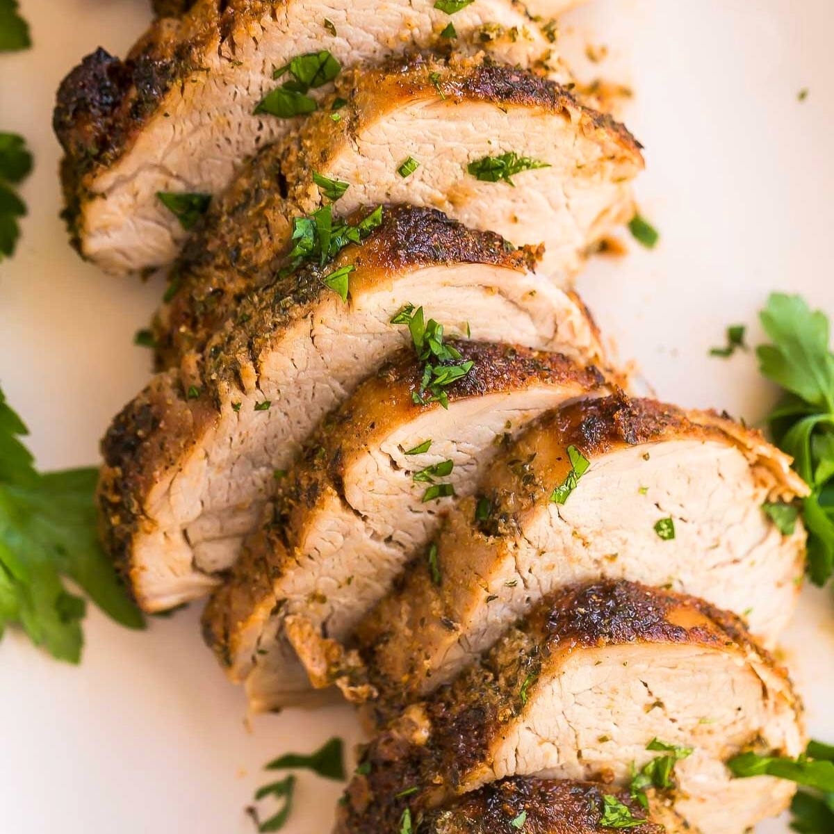 A plate of sliced pork tenderloin. The pork is cooked to a golden brown and looks juicy and tender. It's garnished with fresh parsley.