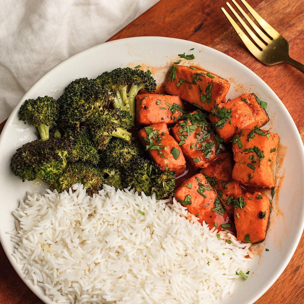 A healthy and colorful meal with salmon, broccoli, and rice. The salmon is cooked in a vibrant red sauce, adding a burst of flavor to the dish.