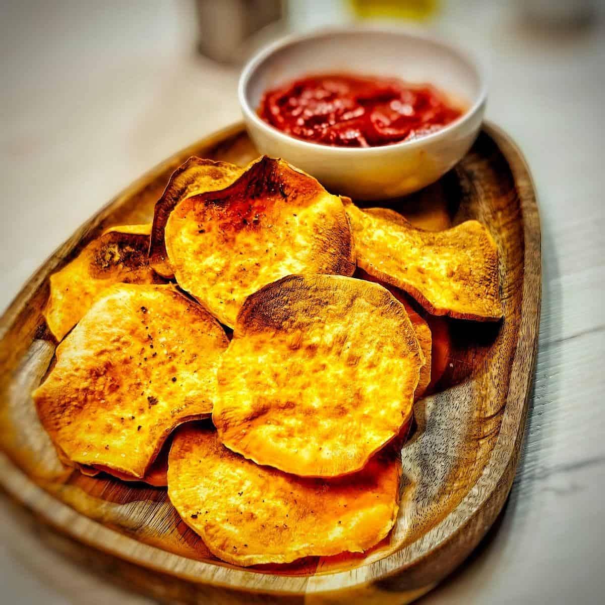 A plate of golden-brown, crispy sweet potato chips served with a side of tomato sauce.