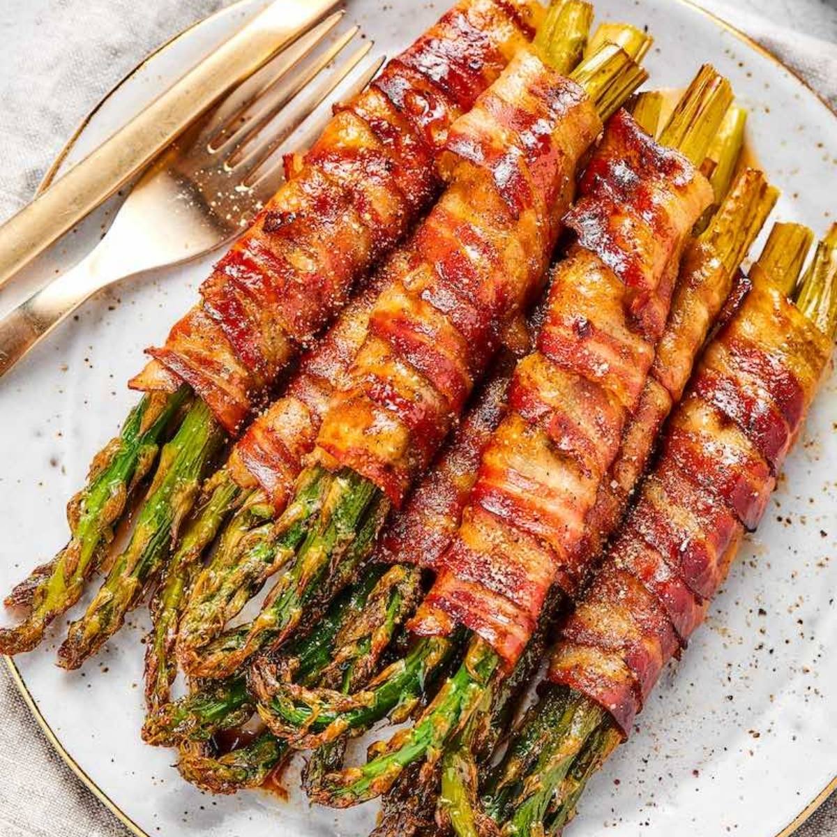 A plate of bacon-wrapped asparagus spears. The asparagus is cooked and the bacon is crispy and golden brown.