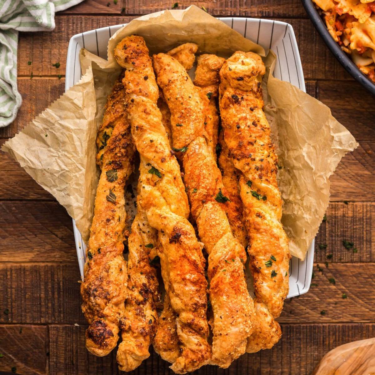 A plate of golden-brown, twisted cheese sticks sprinkled with herbs and spices.