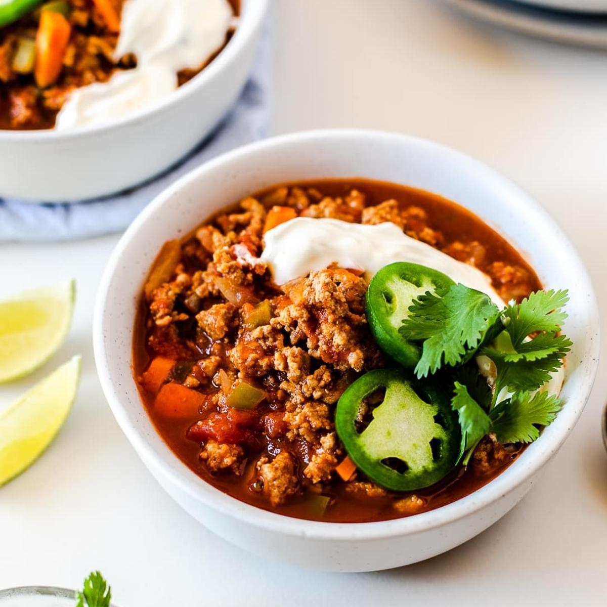 A bowl of hearty chili topped with a dollop of sour cream, chopped cilantro, and sliced jalapeños.