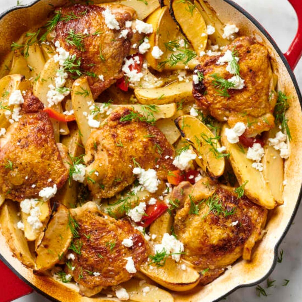 A skillet filled with a delicious Greek-inspired dish. It features tender chicken thighs, roasted potatoes, crumbled feta cheese, and vibrant red bell peppers, all simmering in a flavorful sauce. 