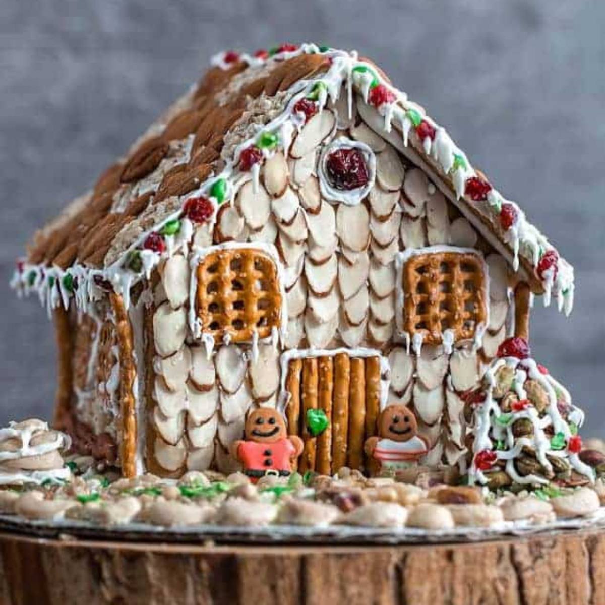 An elaborately decorated gingerbread house with a nut-covered roof, pretzel windows, and two gingerbread men in front.