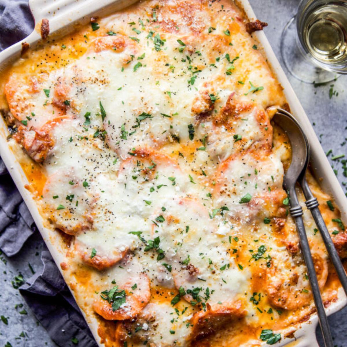 A golden-brown lasagna with melted cheese, herbs, and a side of wine.