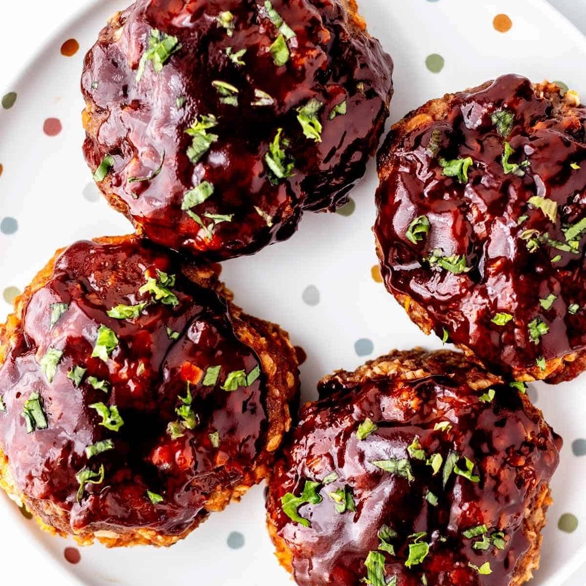 A plate of four mini meatloaves glazed with a rich, savory sauce and sprinkled with fresh parsley.