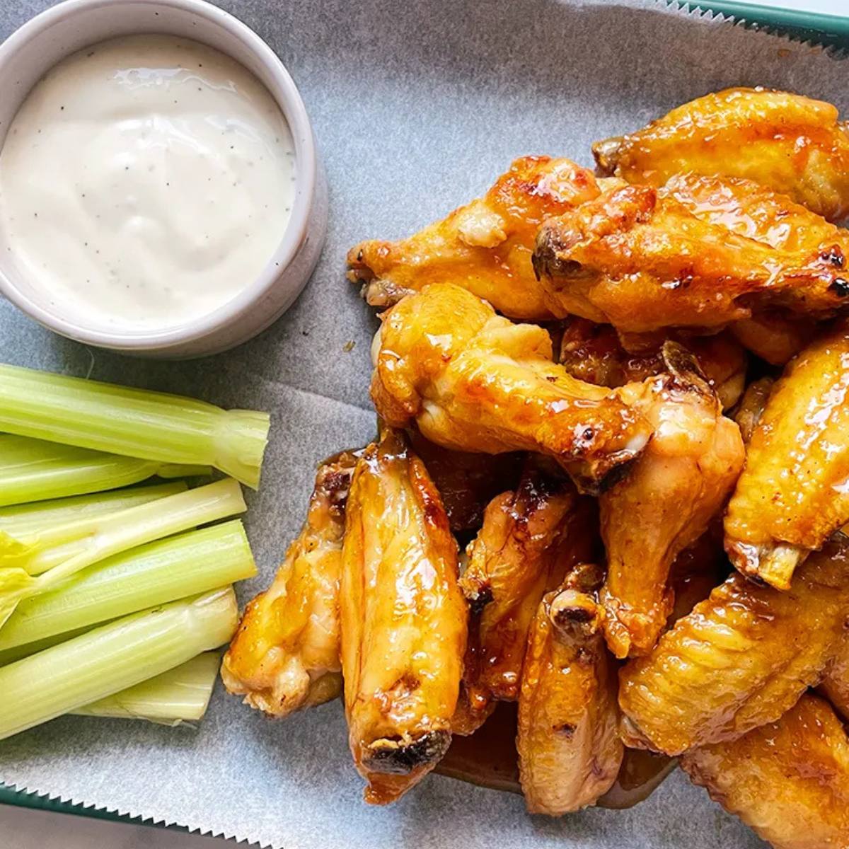 A plate of crispy, golden-brown chicken wings, served with a side of celery sticks and a bowl of creamy blue cheese dressing.