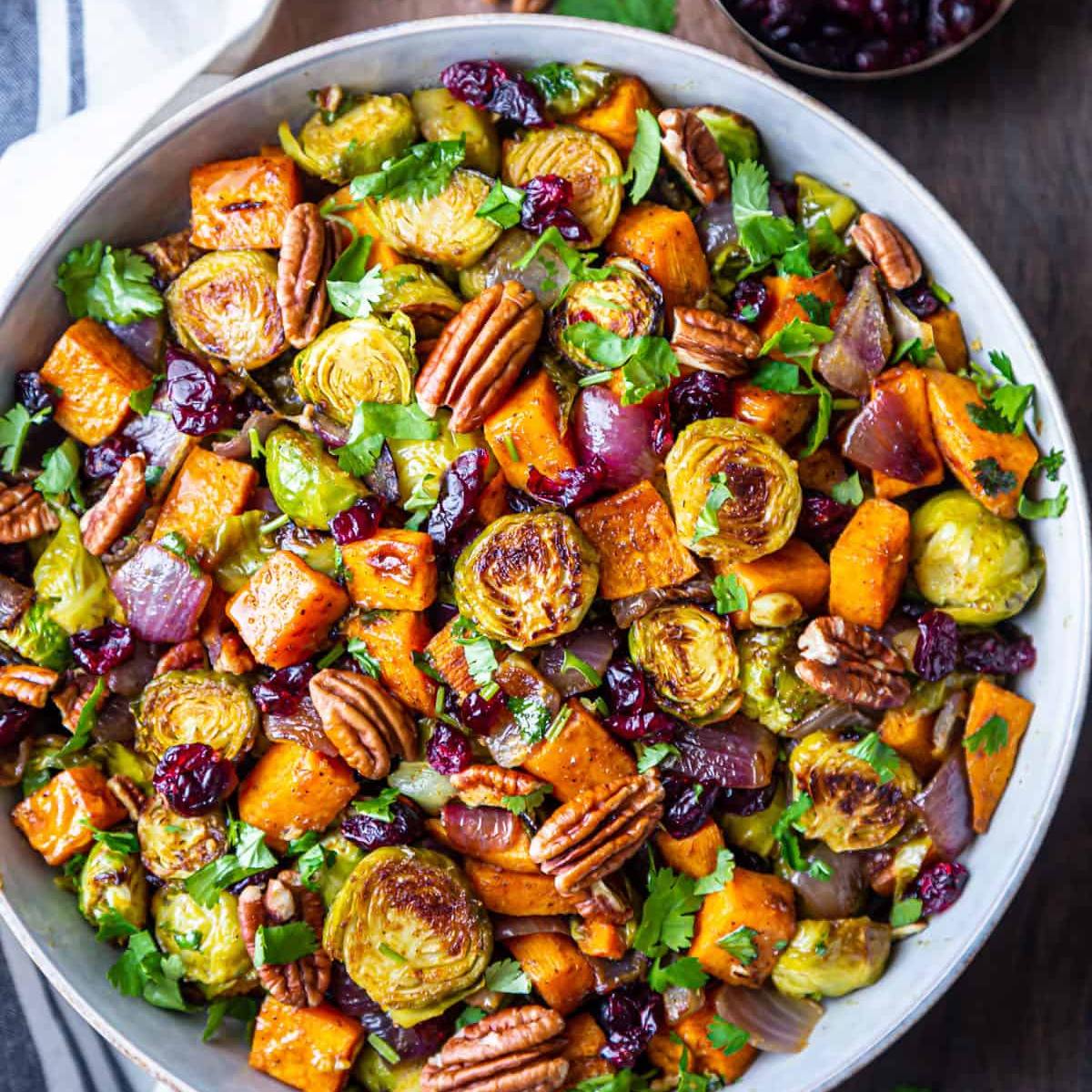 A bowl of roasted Brussels sprouts, sweet potatoes, and onions, topped with cranberries and pecans.