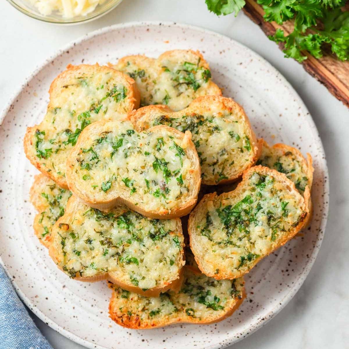 This image shows a plate of garlic bread. The bread is sliced and topped with melted cheese and chopped parsley.