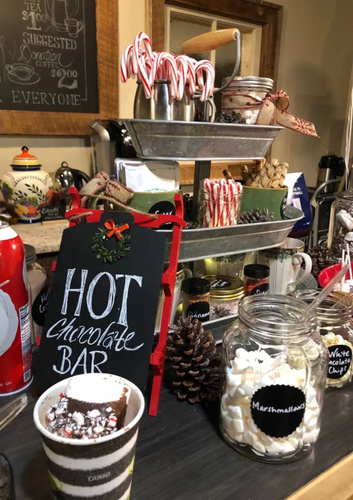 A festive hot chocolate bar with a chalkboard sign, candy canes, marshmallows, and other toppings.