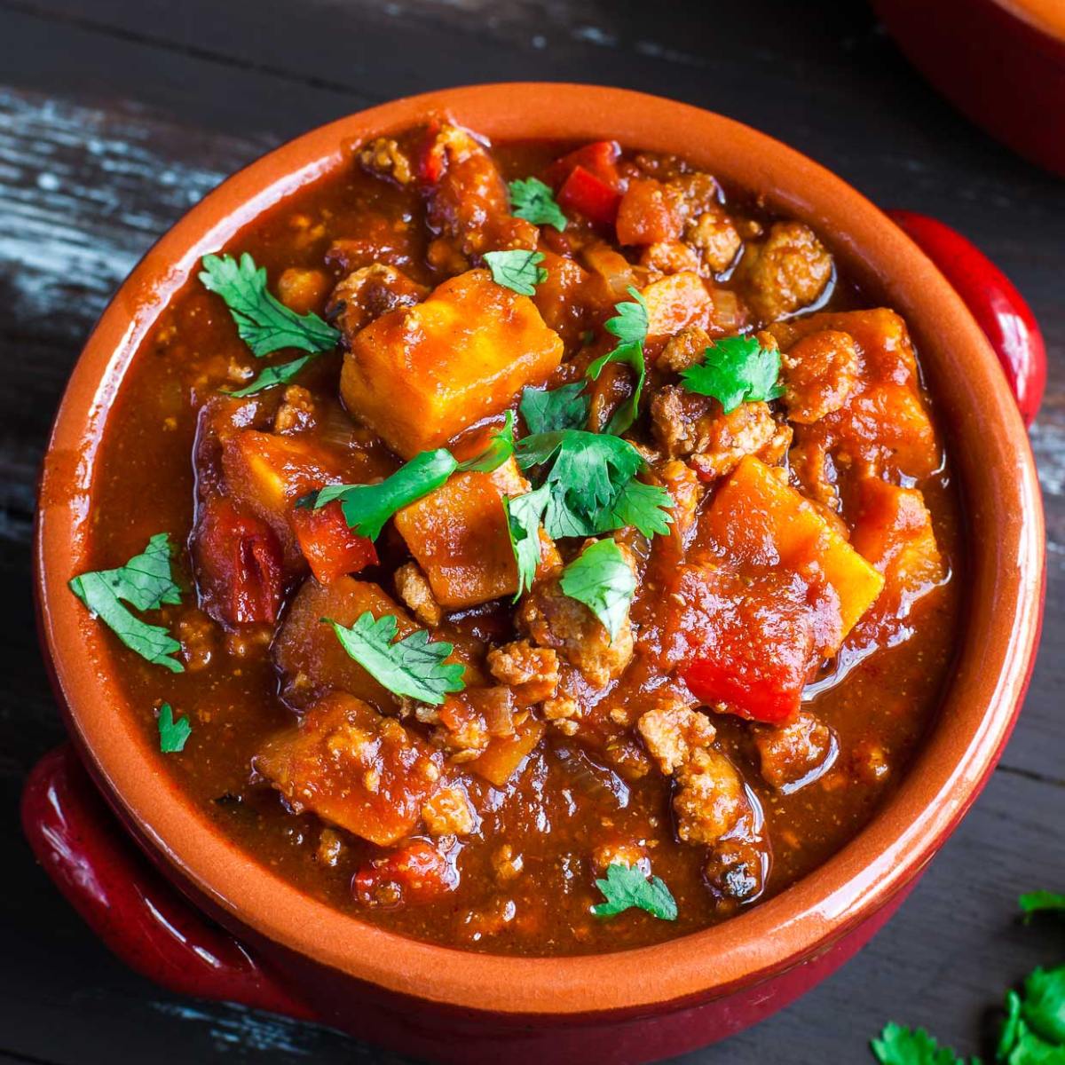 A bowl of hearty chili with sweet potatoes, ground meat, and vegetables.