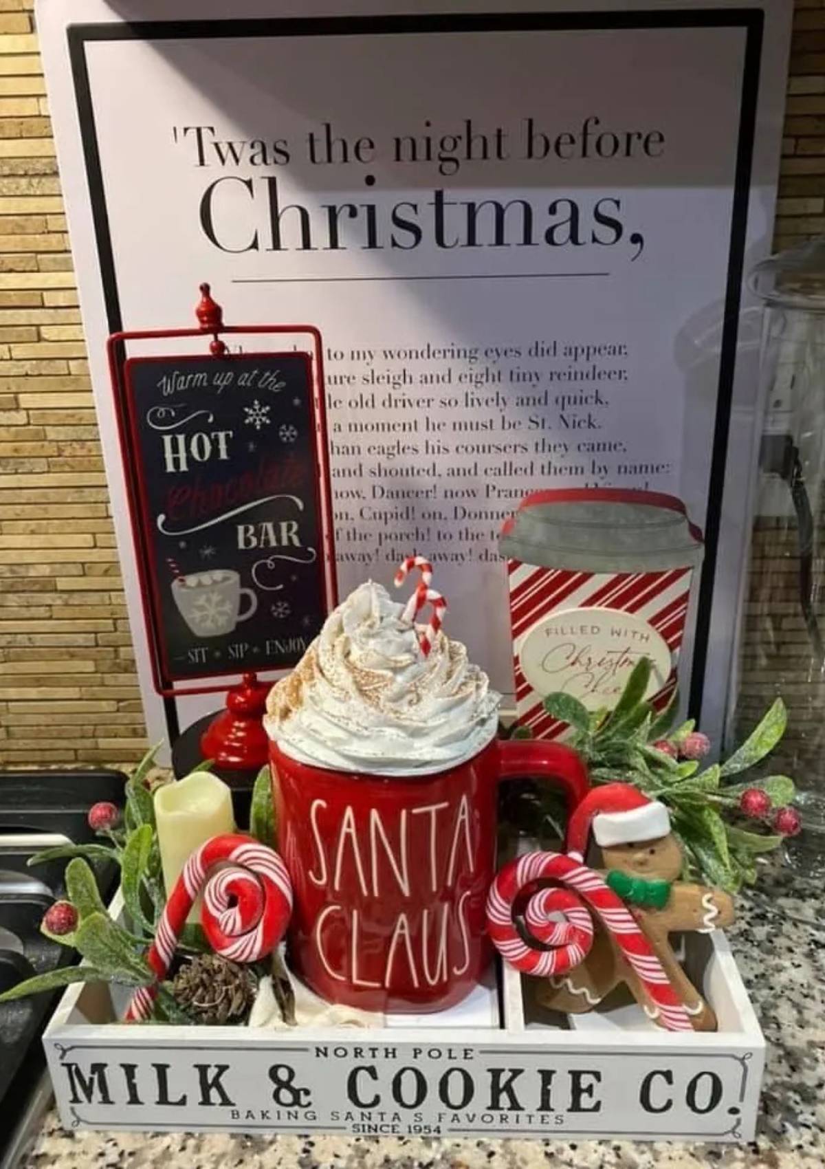 A festive hot cocoa bar with a chalkboard sign that says "Baby it's Cold Outside, Warm Up Here." The bar includes hot chocolate, marshmallows, candy canes, and cookies.