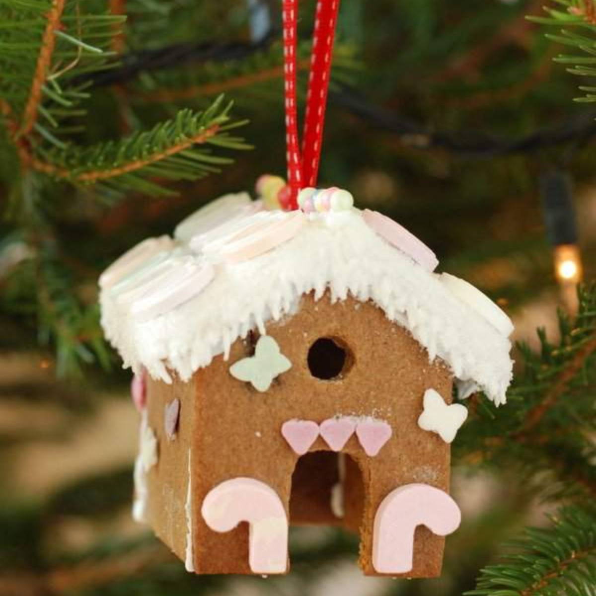 A whimsical gingerbread house ornament decorated with icing and candies, hanging on a Christmas tree.