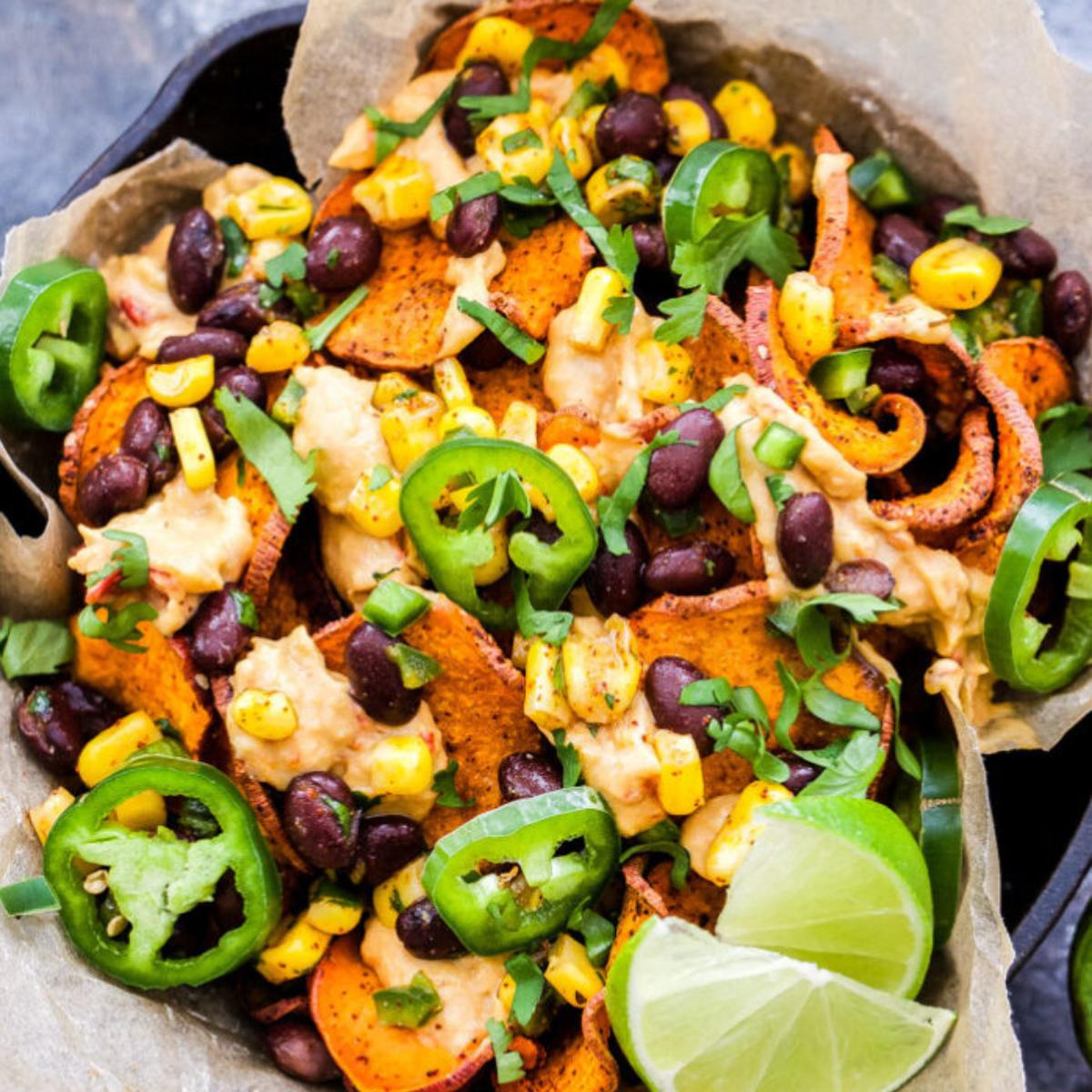 A plate of crispy sweet potato chips topped with black beans, corn, jalapenos, cilantro, and a creamy sauce.