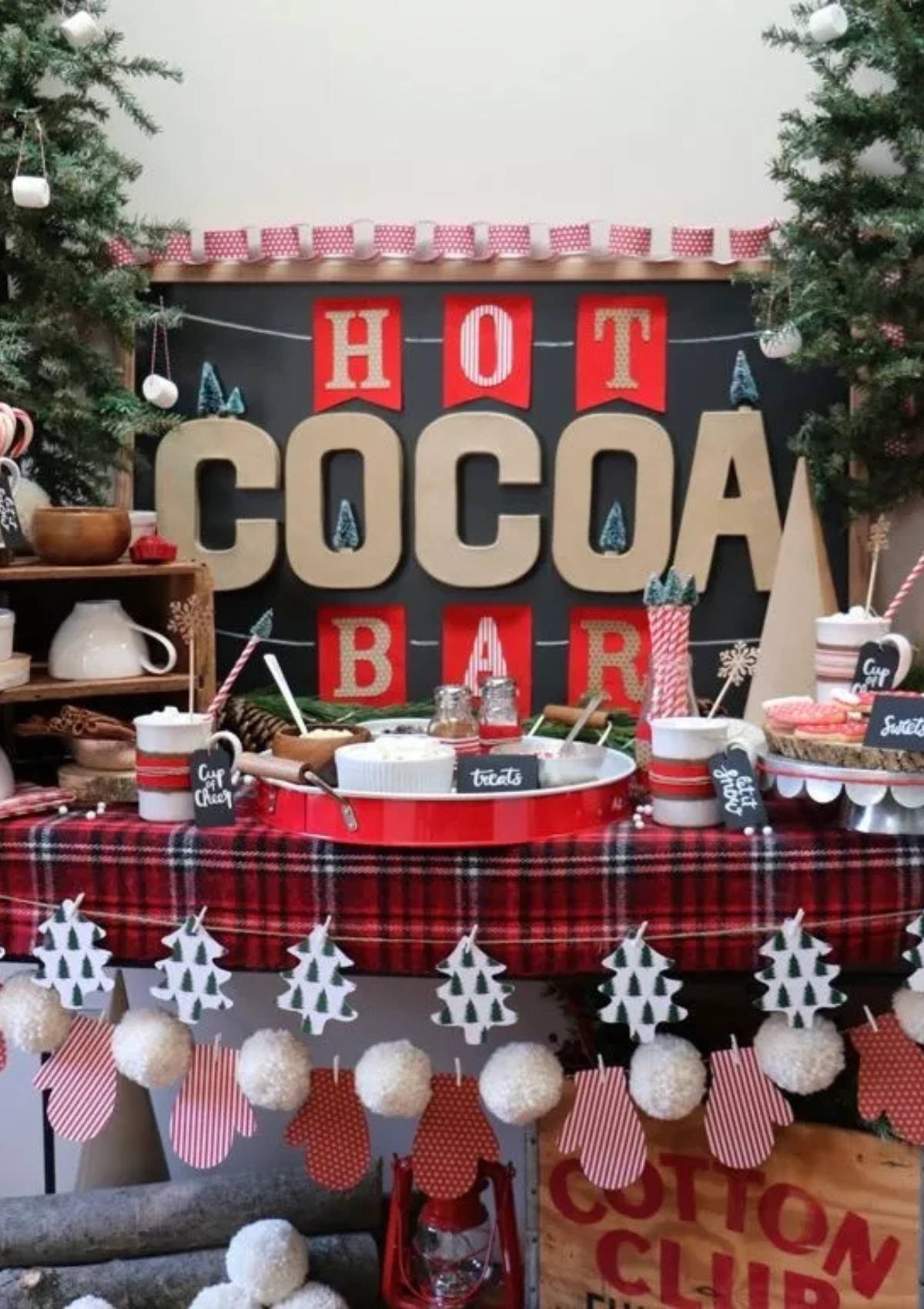 A festive hot cocoa bar with a chalkboard sign that says "Baby it's Cold Outside, Warm Up Here." The bar includes hot chocolate, marshmallows, candy canes, and cookies.