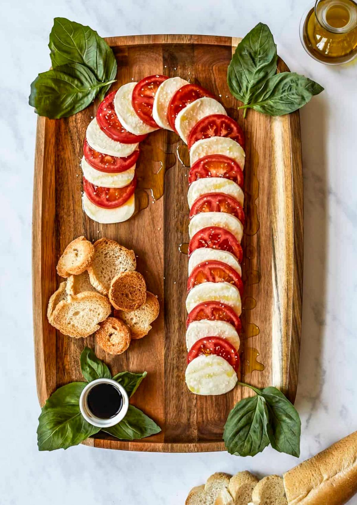 A festive Caprese salad arranged in the shape of a candy cane on a wooden board. The salad consists of alternating slices of fresh mozzarella and ripe tomatoes, drizzled with balsamic glaze.