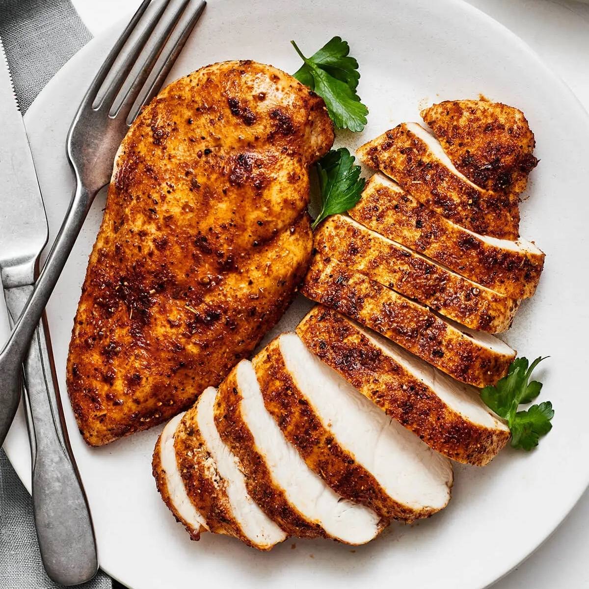 A plate of sliced and whole air fried chicken breasts. The chicken breasts have a golden-brown crust and are seasoned with herbs and spices.