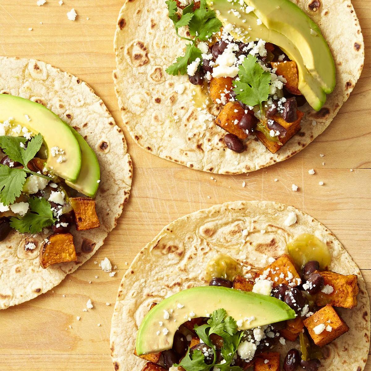 Three soft tacos filled with roasted sweet potatoes, black beans, cheese, avocado, and cilantro.