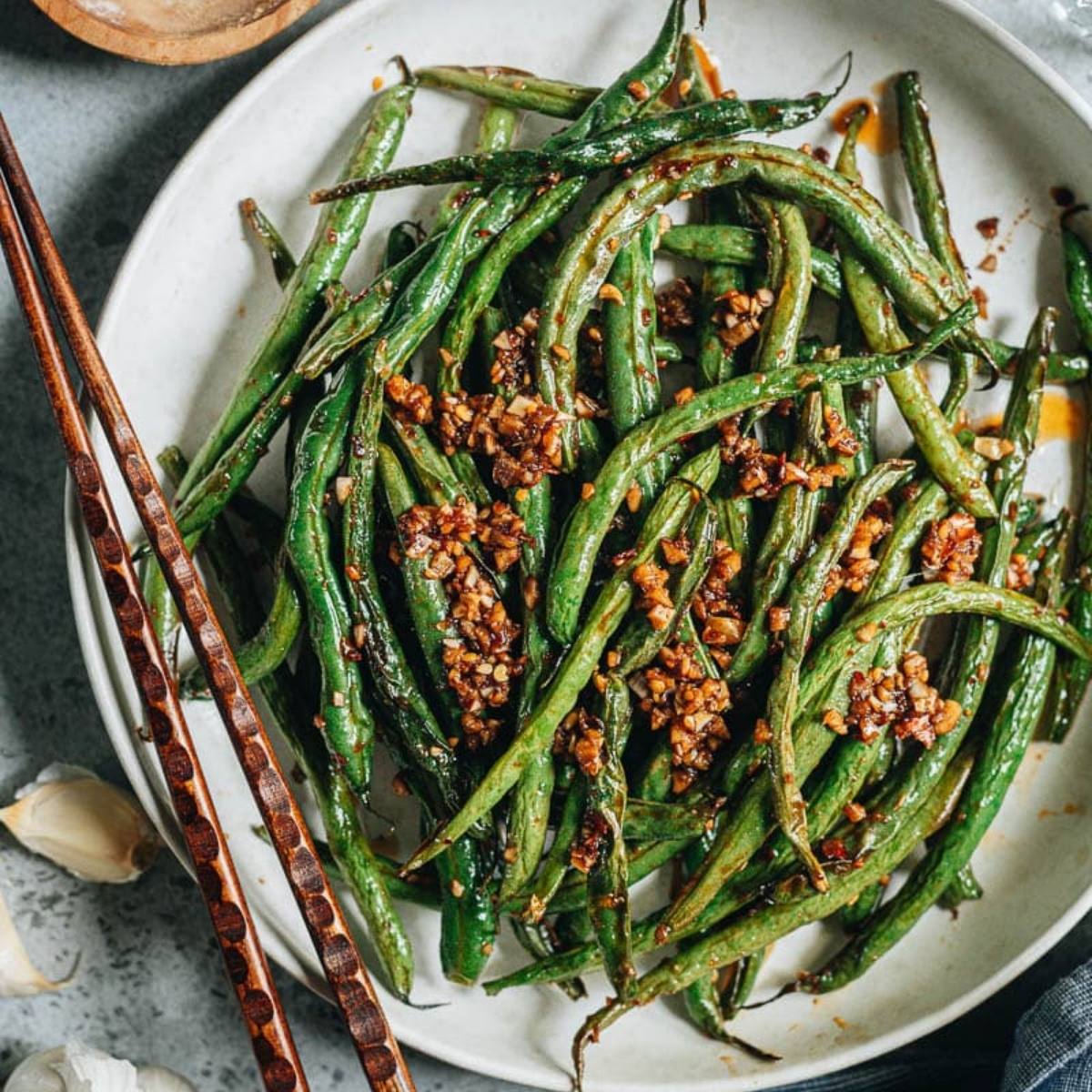 A plate of air fried green beans with garlic and chili flakes. The beans are bright green and look crispy and flavorful.