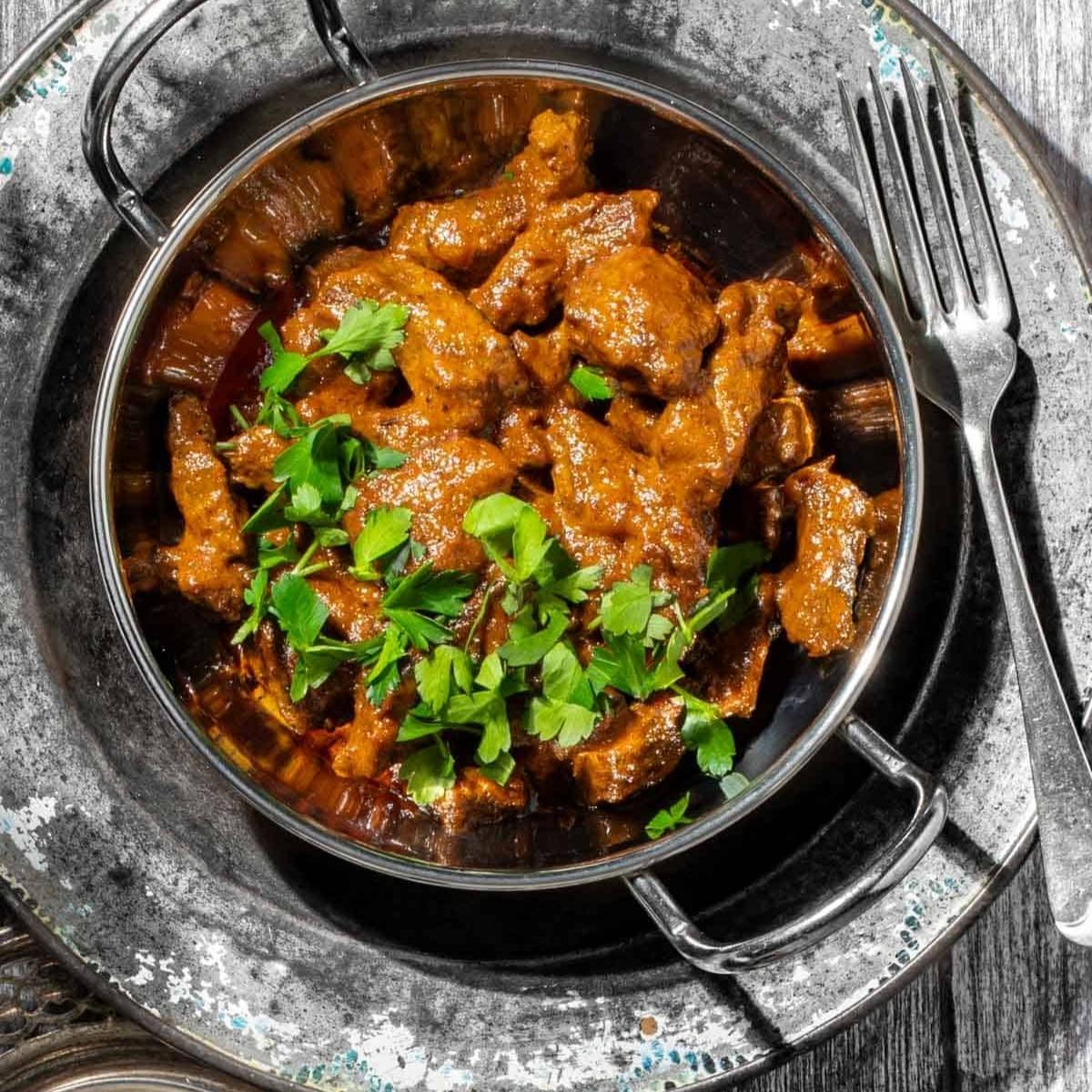 A bowl of rich, aromatic beef curry. The meat is tender and coated in a flavorful, reddish-brown sauce. Fresh parsley is sprinkled on top.