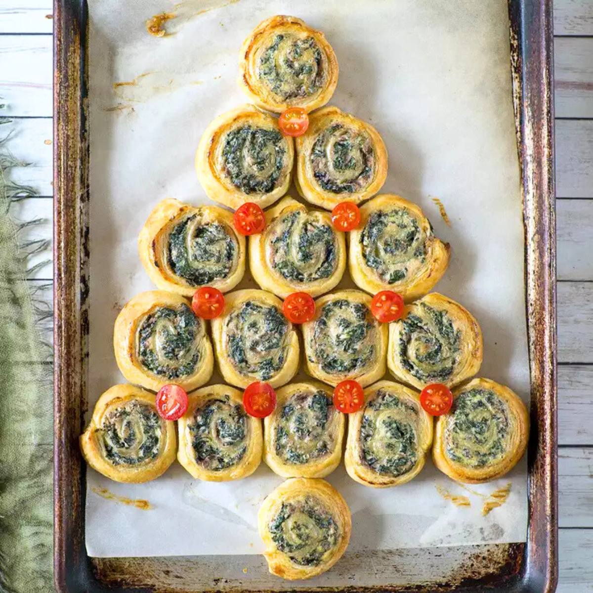 A festive Christmas tree shape made out of spinach and ricotta pinwheels. The pinwheels are arranged in a tree shape and decorated with cherry tomatoes.