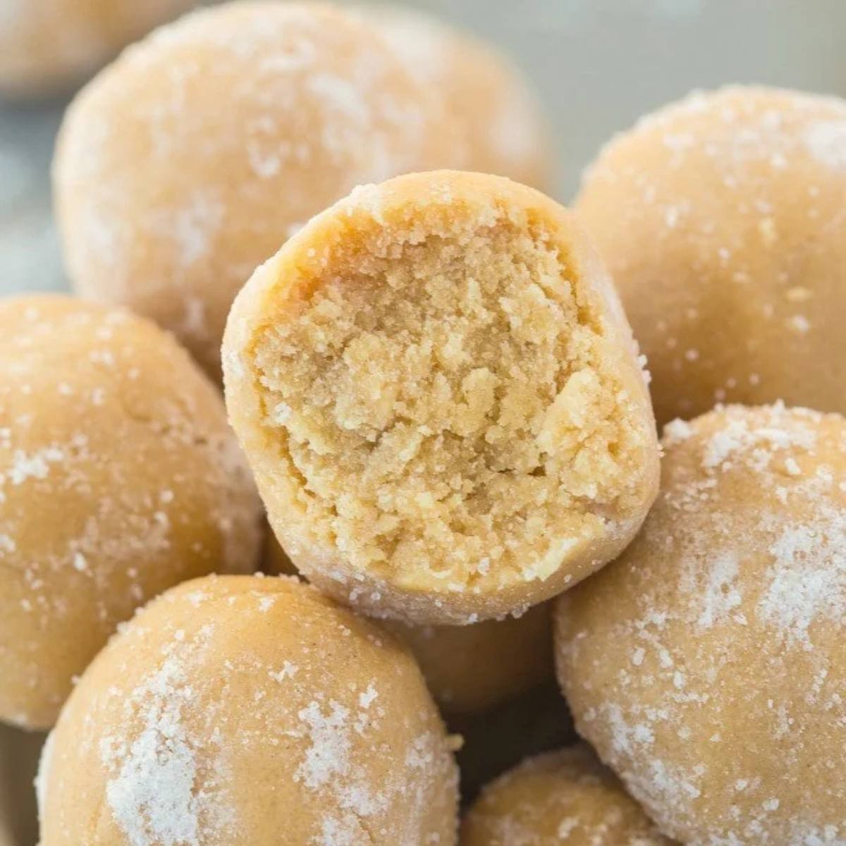 A close-up of peanut butter balls. One of the balls is cut in half, revealing the peanut butter filling. The balls are coated in powdered sugar.