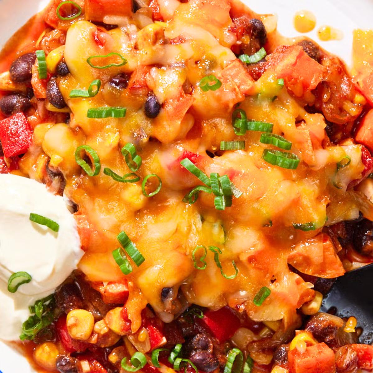 A close-up of a baked dish filled with a hearty chili, topped with melted cheese, sour cream, and green onions.