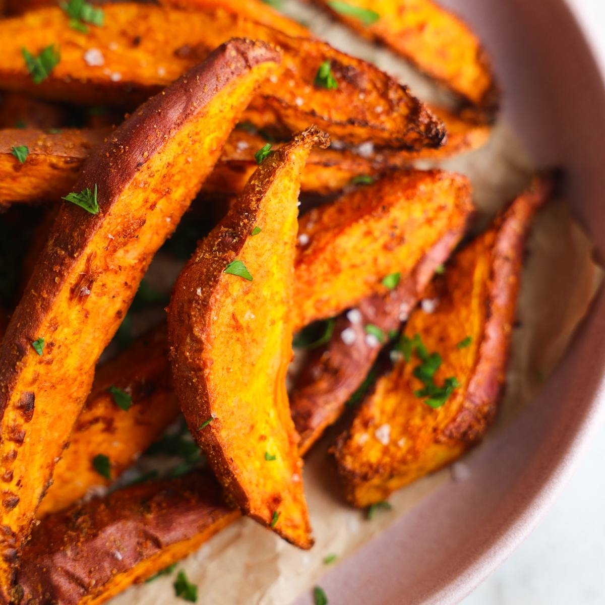 A bowl of crispy, golden-brown sweet potato fries. The fries are sprinkled with salt and parsley, and they look delicious.