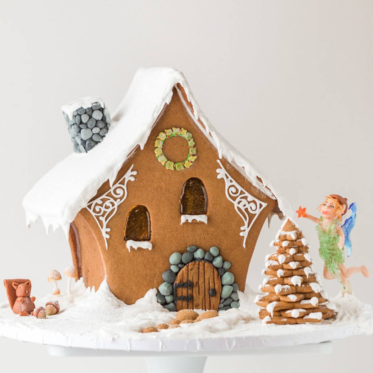 A gingerbread house with intricate details, including a snowy roof, a fairy, a squirrel, and a gingerbread tree.