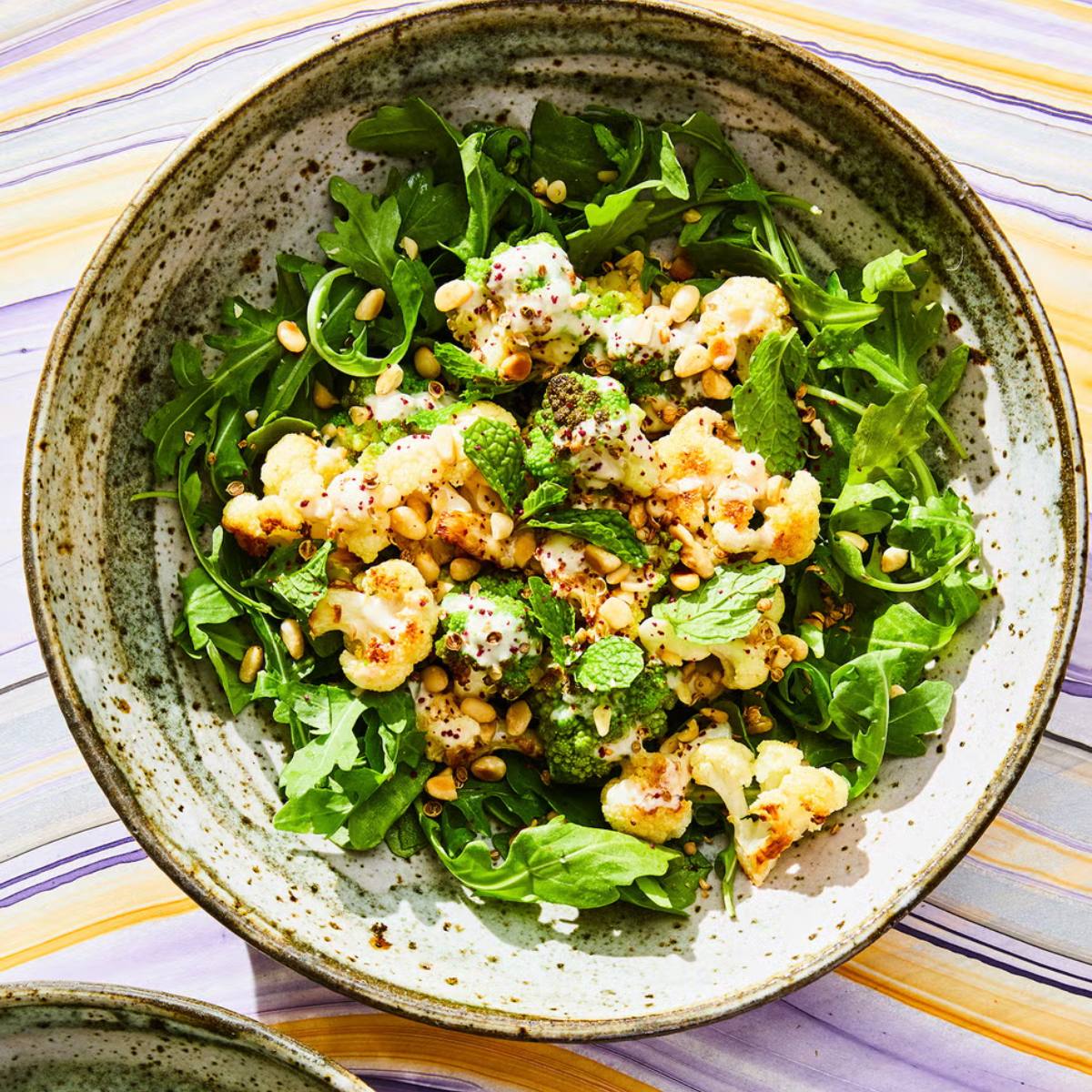 A bowl of roasted cauliflower salad with arugula, mint, pine nuts, and a creamy dressing.