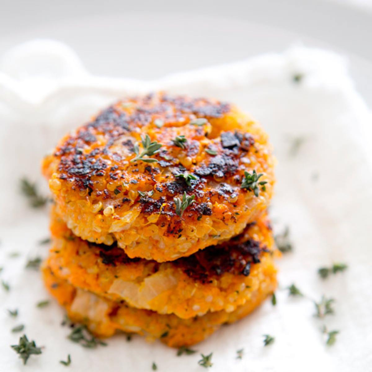 A stack of golden-brown sweet potato quinoa cakes, garnished with fresh thyme.