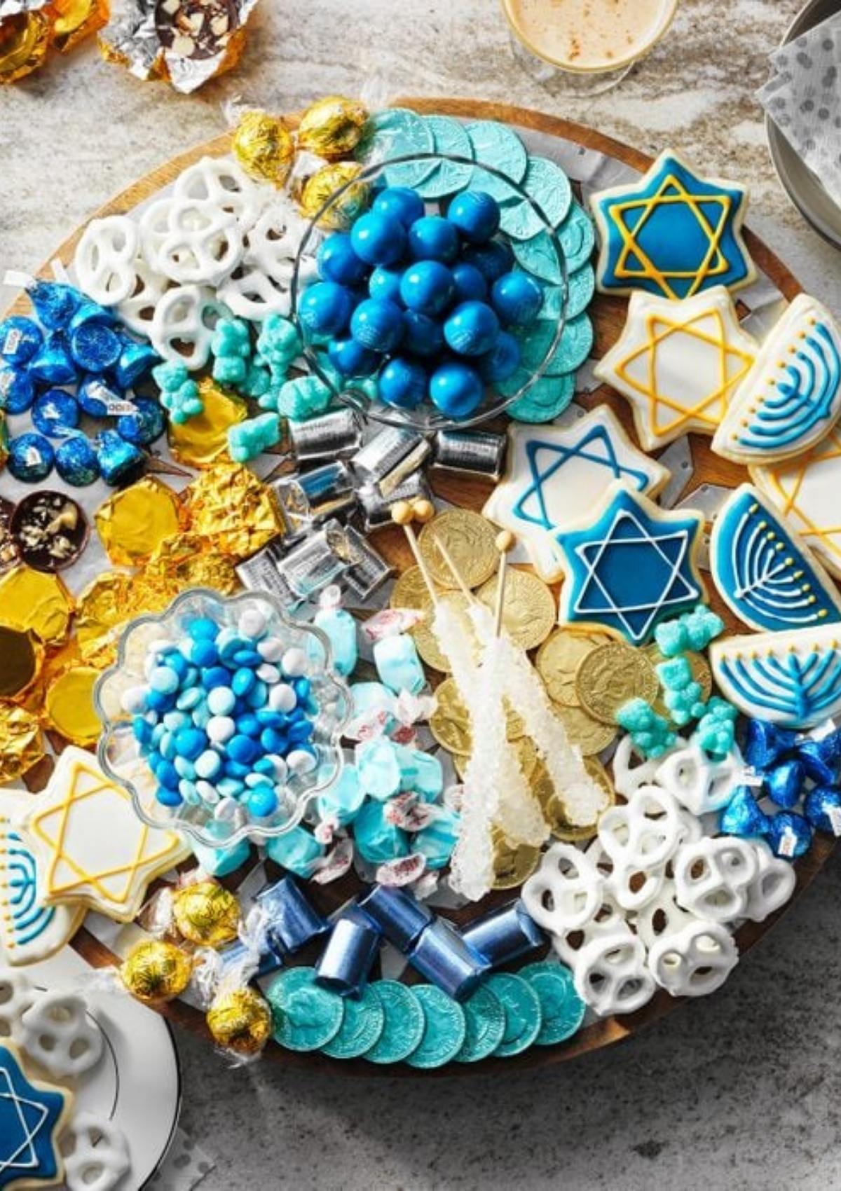 A festive Hanukkah charcuterie board filled with an assortment of blue and white candies, chocolate coins, pretzels, and cookies decorated with Stars of David and menorahs.