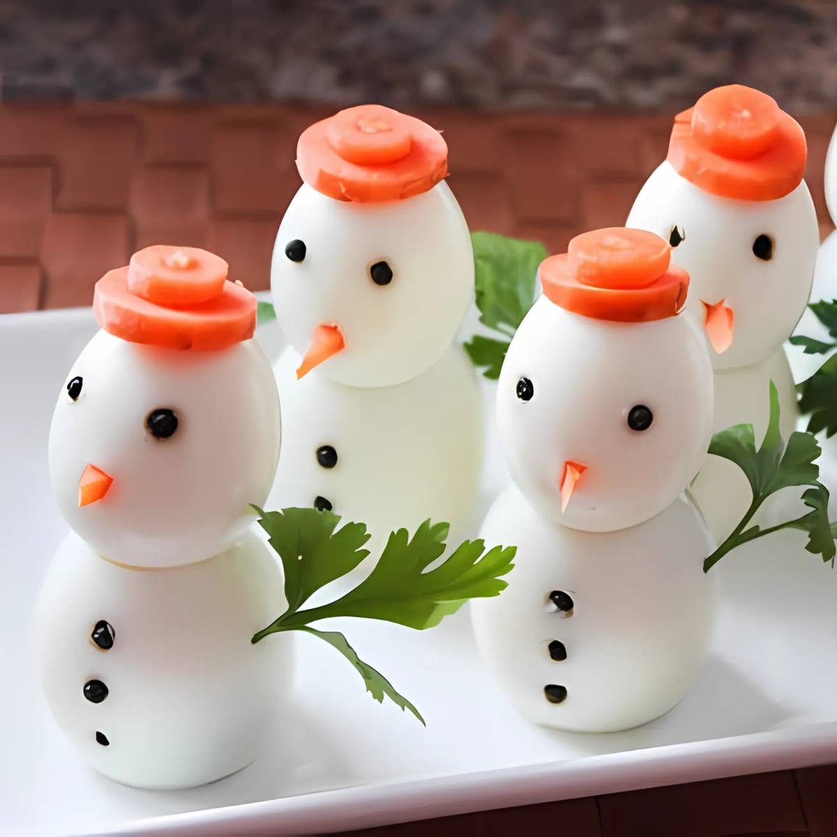 A plate of adorable snowman-shaped deviled eggs. The eggs are stacked in twos, with carrot slices as hats and peppercorns as eyes and mouths. A sprig of parsley adds a festive touch.