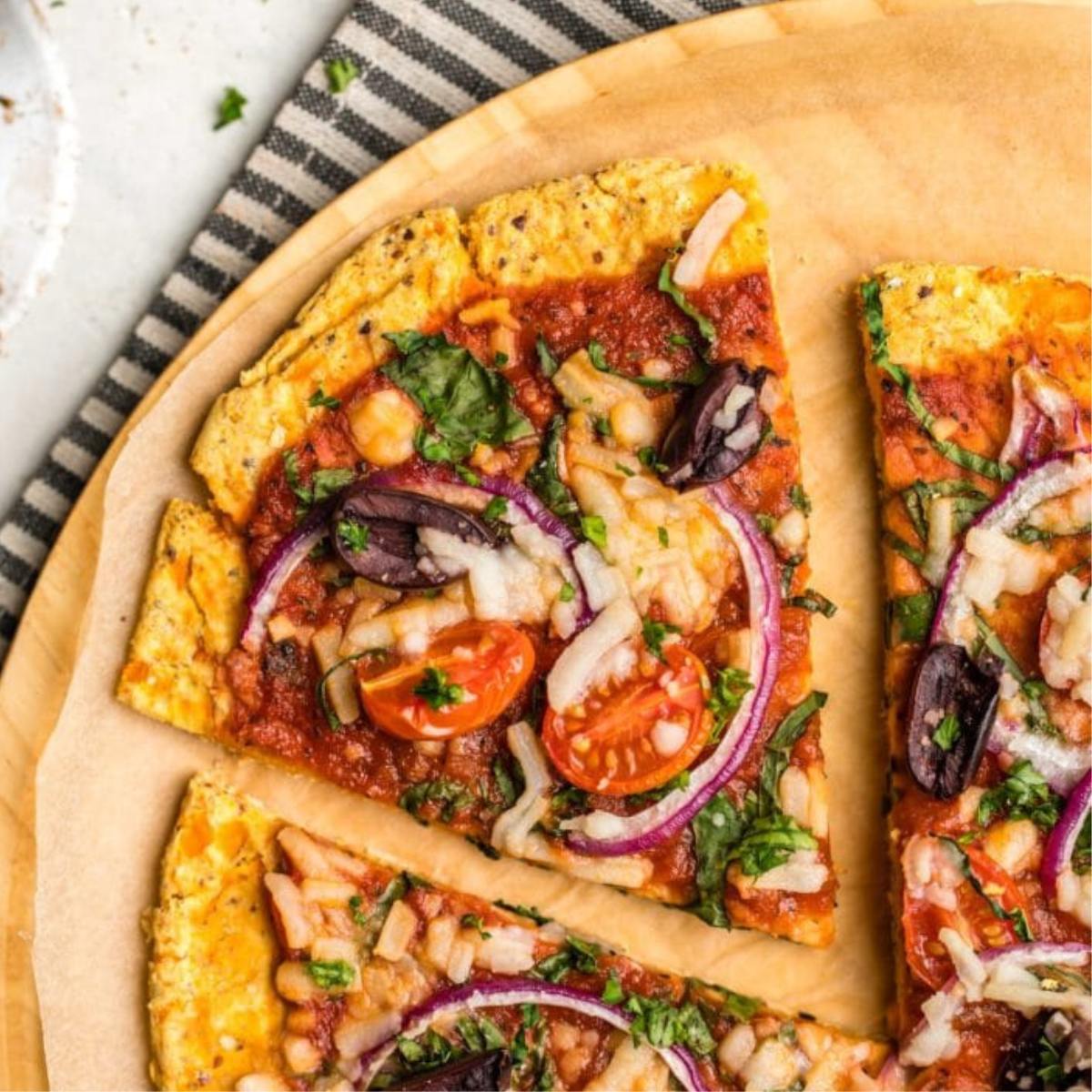 A slice of vegan pizza with a chickpea crust, topped with tomato sauce, vegetables, and cheese.