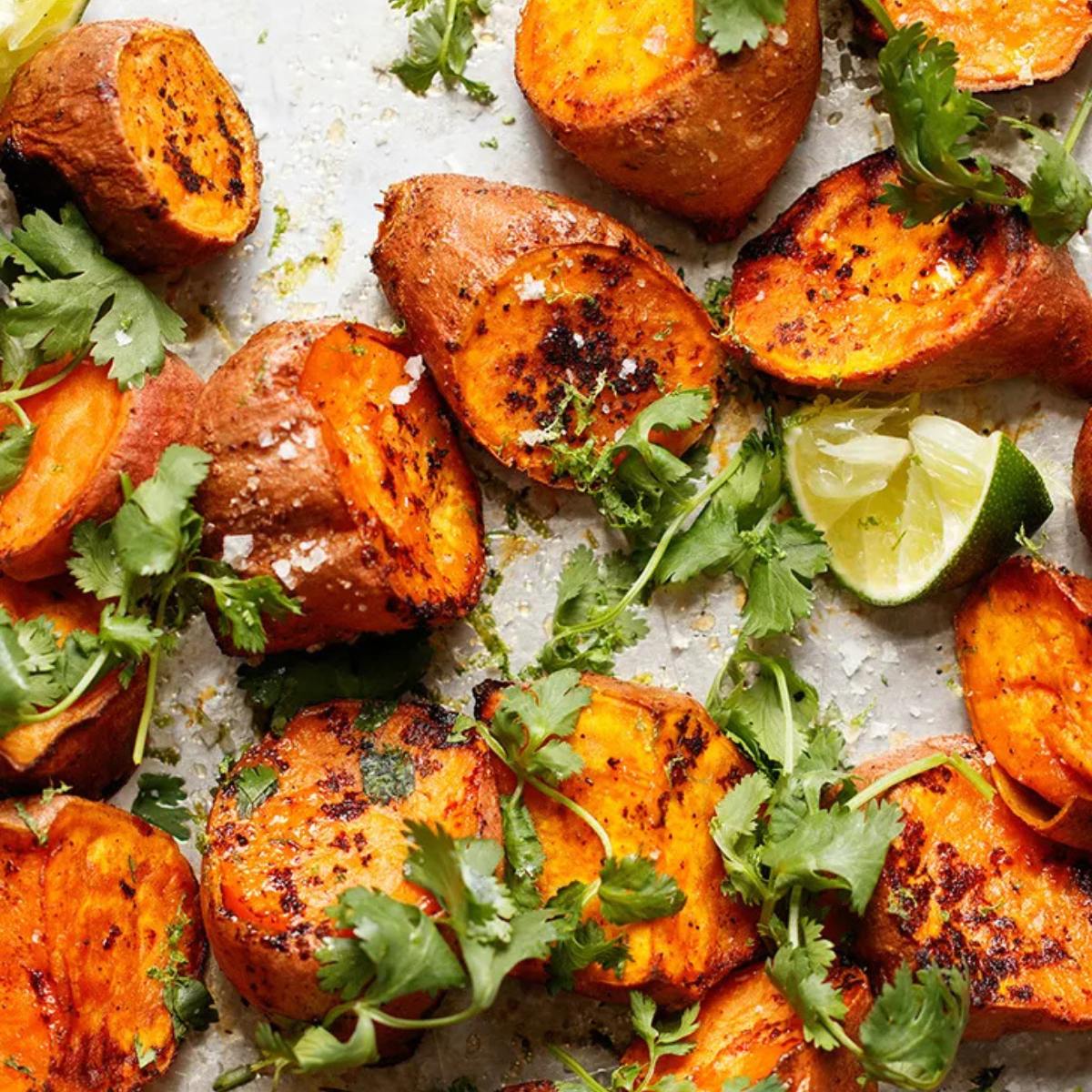 A close-up of roasted sweet potato wedges seasoned with spices and topped with fresh cilantro and lime wedges.