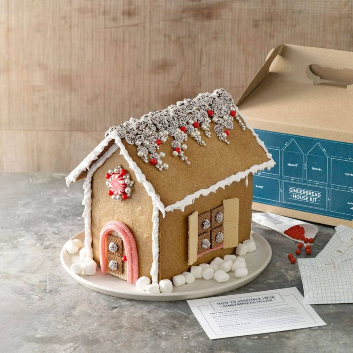 A festive gingerbread house assembled from a kit, decorated with icing, candies, and marshmallows.